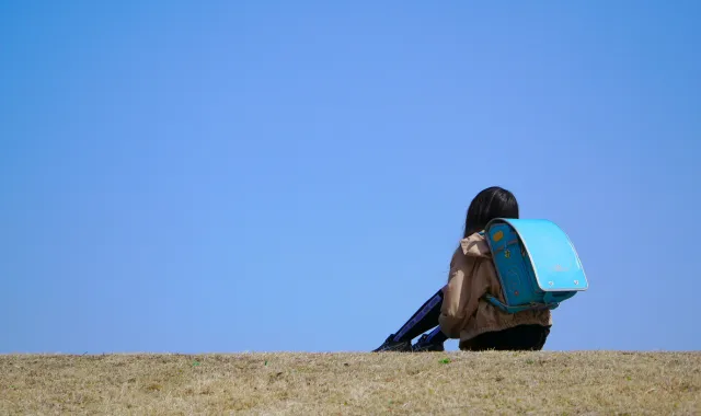 水色のランドセルを背負って空を見つめる小学生の女の子